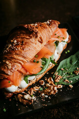 Gourmet croissant sandwich with smoked salmon. Croissant filled with smoked salmon, spinach and cream cheese. Styled with rustic textures for brunch, bakery and gourmet food branding