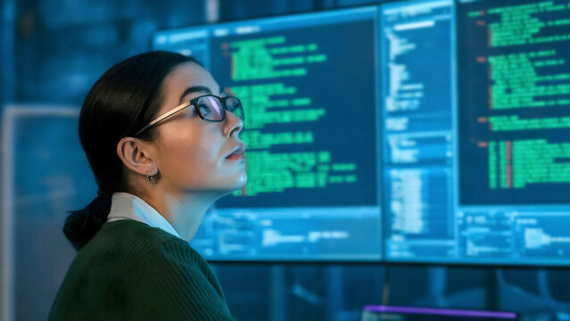 Focused young programmer intently analyzing code on multiple screens in a modern tech office setting