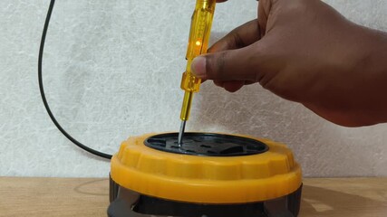 Closeup of Indian electrician hand checks presence of electrical voltage in socket phase using an electrical tester screwdriver. Examining wires in electrical outlet by voltage detector.