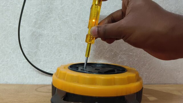 Closeup of Indian electrician hand checks presence of electrical voltage in socket phase using an electrical tester screwdriver. Examining wires in electrical outlet by voltage detector.