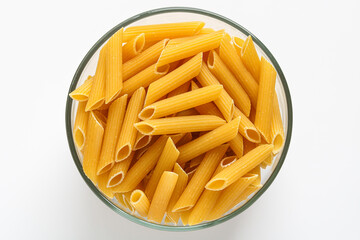 Top view of uncooked penne pasta in a clear glass bowl, presented on a clean white background.