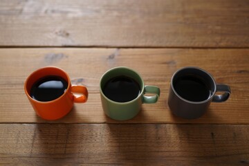 Three colorful coffee mugs filled with dark coffee on a wooden table
