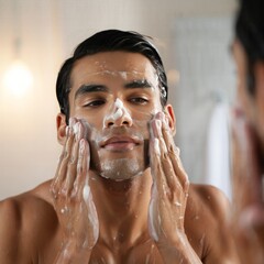 Man washing his face with cleansing foam in the bathroom mirror