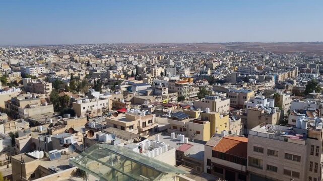 Panoramic skyline view over Madaba, Jordan, with morning sun illuminating rooftops and the city stretching across rolling hills toward the distant horizon