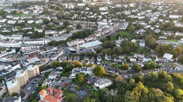 Cinematic aerial drone view of Torquay town center showcasing residential buildings streets trees and urban landscape during early morning in Devon England