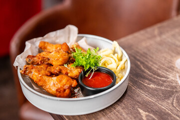 A bowl of crispy fried chicken wings served with a dipping sauce and garnish on a rustic wooden table, shot from a high angle