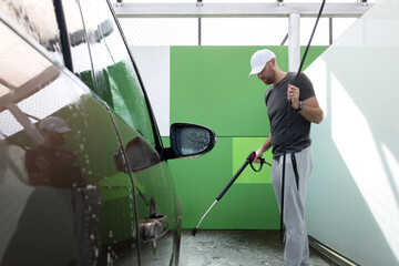 Young man washing car with a hose