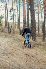 Fototapeta premium Young boy riding a BMX bike on a dirt path through a serene pine forest on an overcast day, enjoying outdoor activity and nature.