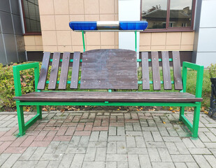 Police light bar mounted above park bench, urban setting, security equipment over seating, public space furniture, law enforcement symbol over resting area, city infrastructure detail