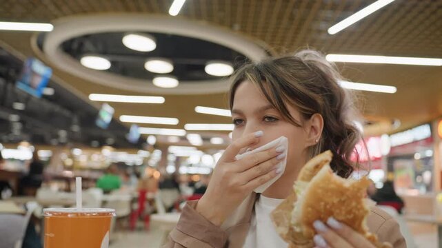 youthful woman coughs, concerned young woman coughs during busy shopping mall lunch, casual scene shows young woman experiencing coughing episode in crowded shopping mall dining area