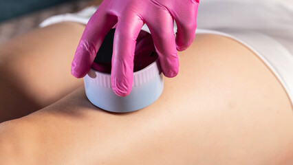 The hand of a cosmetologist makes an anti-cellulite massage with a portable vacuum massager, close-up, effective