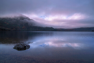 Muckross Lake serene landscape on a winter morning after rain, with fogs and drifting clouds over Shehy Mountain in Killarney National Park, Ireland, a Zen‑like sunrise tranquility and relaxation.