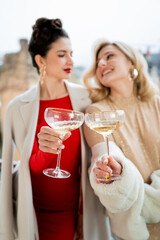 Two young women in festive dresses and with glasses of champagne in their hands celebrate the New Year and Christmas.