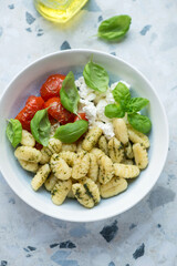 Plate of italian gnocchi with roasted tomatoes, ricotta cheese and basil, vertical shot on a white and blue granite background, elevated view