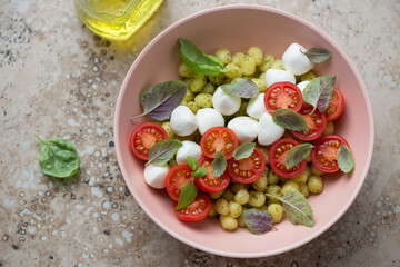 Roseate bowl with italian chicche di patate served in caprese style, horizontal shot on a beige granite background, high angle view