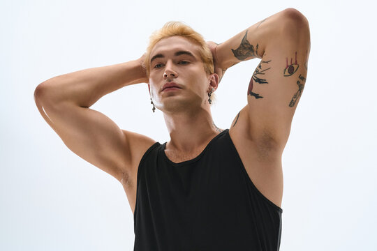 Handsome young man poses with arms raised, displaying his fashionable style and tattoos.