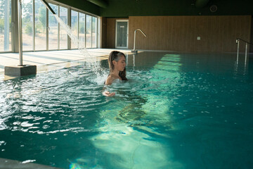 Woman relaxing under waterfall in modern spa pool