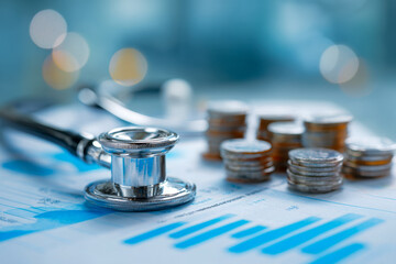 Stethoscope and stacked coins placed on financial charts symbolizing healthcare costs and medical economics with blurred background lights