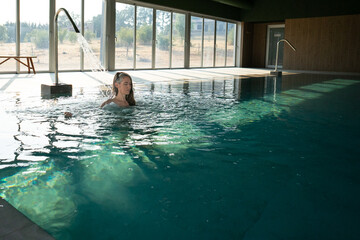 Woman relaxing under waterfall in indoor swimming pool
