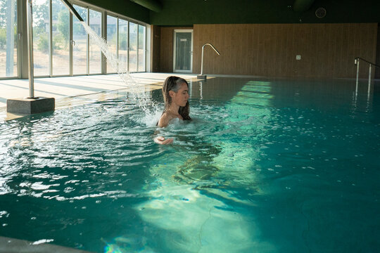Woman relaxing under waterfall in modern spa pool