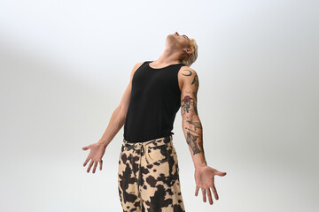 Confident young man poses stylishly in a trendy outfit against a simple backdrop.