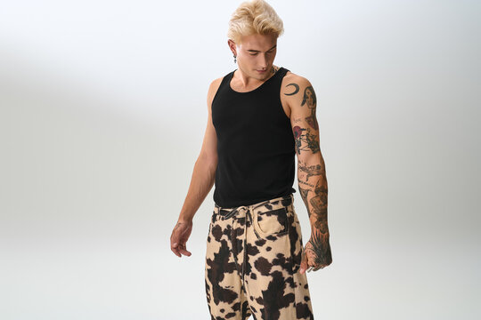 Handsome young man in a tank top and patterned pants striking a posed look in a bright studio.