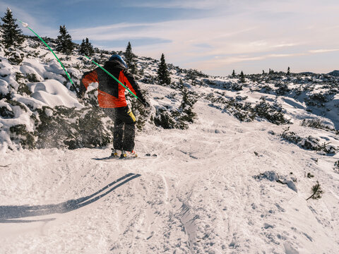 A skier in an orange jacket and blue helmet skis down a snowy slope, kicking up snow with their poles. Paganella, Roda refuge,Trentino, Italy
