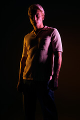 Young man stands confidently in stylish attire with colorful lighting enhancing the vibe.