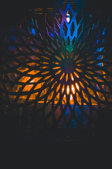 Abstract glowing pattern with colorful light shining through a decorative metal lattice. Vibrant blue and orange tones create a mystical, artistic atmosphere.