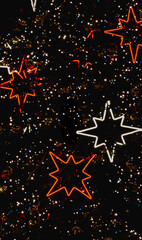 Colorful Christmas stars and sparkling bokeh lights forming a festive holiday background. Warm glowing red and white shapes on a dark backdrop.