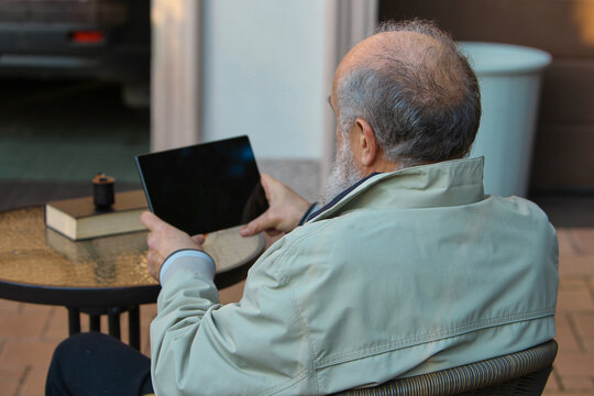 Senior man relaxing outdoors with tablet at patio table in peaceful mood. Concept of lifestyle leisure, senior technology use, home comfort scenes, and calm everyday moments.