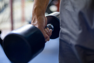 Fototapeta premium Close-up of a strong hand gripping a black dumbbell in a gym setting, representing fitness, strength training personal health goals in a modern lifestyle context.