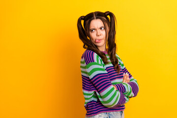 Playful young woman with colorful striped sweater stands against yellow background crossing arms sticking out tongue for a fun casual fashion