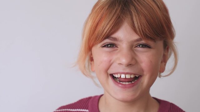 Closeup portrait face of happy caucasian girl elementary school blond ginger redhead hair, smiling, grey eyes. Looking at camera. Positive mood, joyful, cheerful kid child, laugh over white background