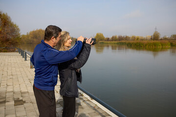 Middle-aged woman with a friend on the shore of a water looking for birds through binoculars
