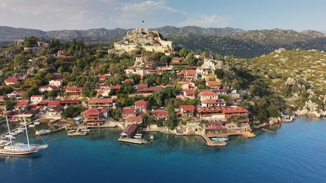 Aerial view of stunning coastal village of Kalekoy, Turkey, showcasing its historic castle, vibrant homes, and crystal-clear waters. Simena castle on the mountain