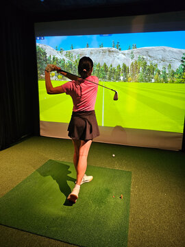 Young golfer practices swing at indoor simulation facility with virtual course in the background concept