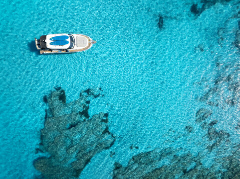 Aerial view of a white yacht floating in clear turquoise Mediterranean sea above rocky seabed, summer vacation scene near Mallorca, Balearic Islands, Spain. Top drone view of boat and azure water