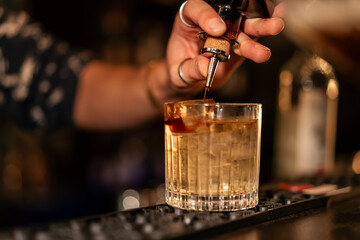 A cocktail being mixed and carefully finished in a bar, presented under warm candlelight.