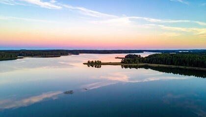 Aerial view of a lake at sunset. The sky is filled with vibrant colors reflecting on the calm water. Trees line the shores, creating a peaceful and serene lands