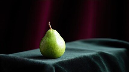 A single green pear sits on a dark green velvet cloth, with a dark background and dramatic lighting.