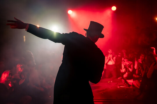 Performer wearing a tailcoat, top hat, and garters stands in the fog during a show, surrounded by an enthusiastic audience.