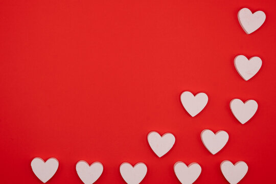 White wooden hearts arranged diagonally in the corner on a bright red background, creating a minimal romantic composition with empty copy space