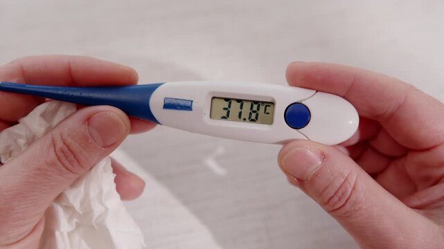 Digital medical thermometer in hand showing elevated body temperature of 37.8 degrees Celsius on electronic display close-up