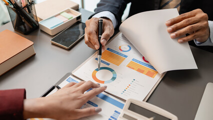 Business professionals meeting at a modern office table, reviewing charts and budget reports while discussing key financial insights and strategic plans for upcoming business decisions.