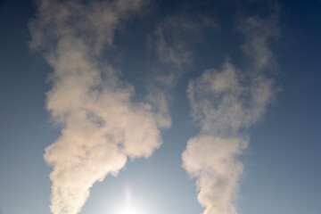 smoke coming from a wide pipe against a blue sky , white steam coming from a pipe during heating of a large industrial premises in cold weather
