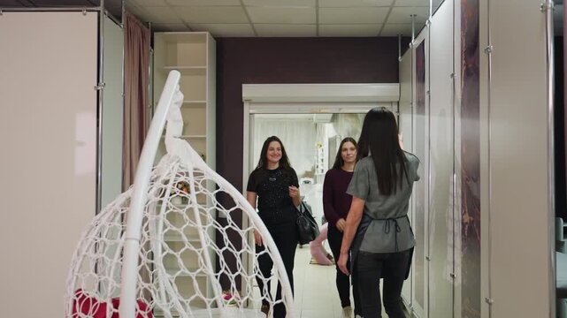 clients pass stylist with cheerful exchange, casual greetings occur as clients walk by stylist, three visitors casually stroll through salon corridor exchanging greetings with stylist on duty