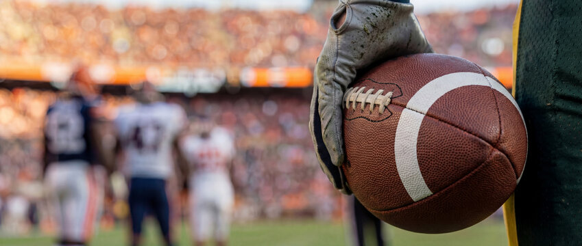 Copyspace, Player gripping an american football on the sideline during a stadium game at sunset, competitive sports action and team strategy atmosphere for fall season athletics and fan energy