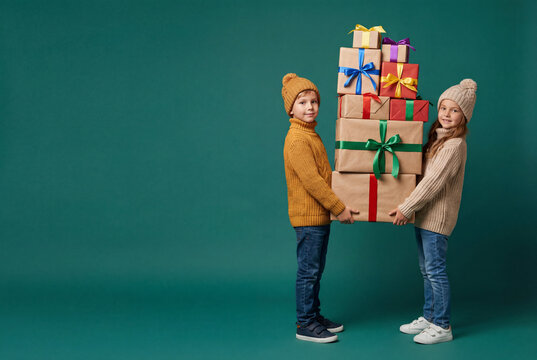 Copyspace, Children carrying a tall stack of wrapped gifts against green studio background, winter holiday spirit and family celebration with playful teamwork and festive giving