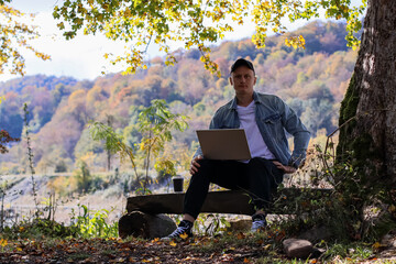 Man leans forward engaged with laptop amid colorful fall leaves and trees